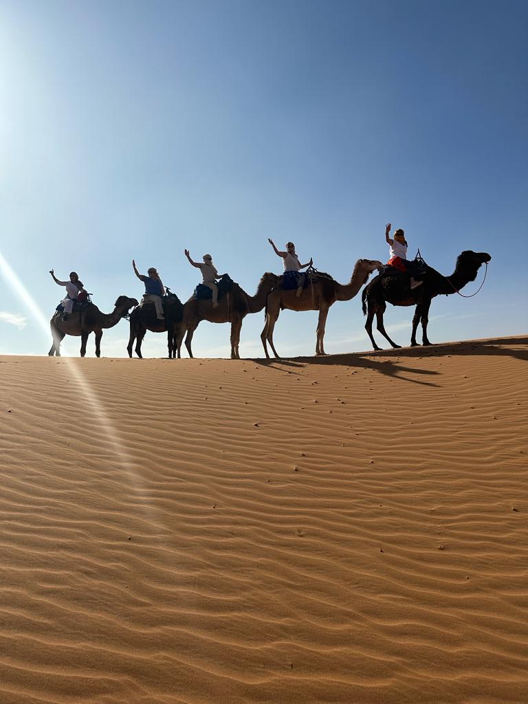 Viajeras saludando desde camellos en las dunas del desierto